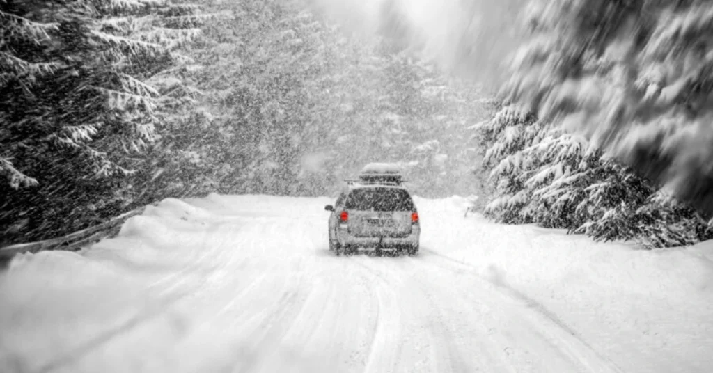 Car traveling on a snow-covered road in a forest during a snowstorm