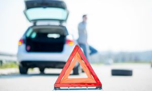 A motorist calls for free roadside assistance for gas behind a car problems warning sign.