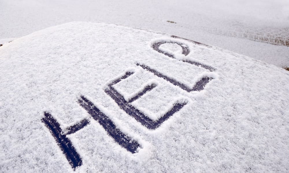 The word “Help!” written into the snow on top of a car.