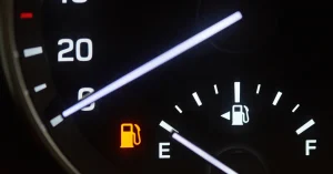 Close-up of a car fuel gauge with the needle on empty and the low fuel warning light illuminated, symbolizing a car running out of gas.
