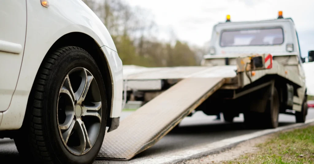 White car being loaded onto a flatbed transport truck for shipping