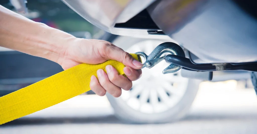 Hand attaching a yellow tow strap to a vehicle's tow hook for secure towing