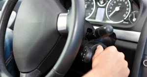 Close-up of a driver’s hand turning the ignition key in a modern car, with dashboard lights visible—commonly associated with car struggling to start or ignition issues