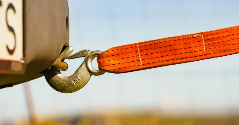 Close-up of a heavy-duty orange tow strap with a metal hook attached to a vehicle’s rear hitch, used for towing or vehicle recovery situations