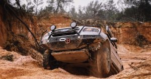 Off-road SUV stuck at an angle on rugged, muddy terrain in a canyon-like area, showing the need for off-road recovery assistance.